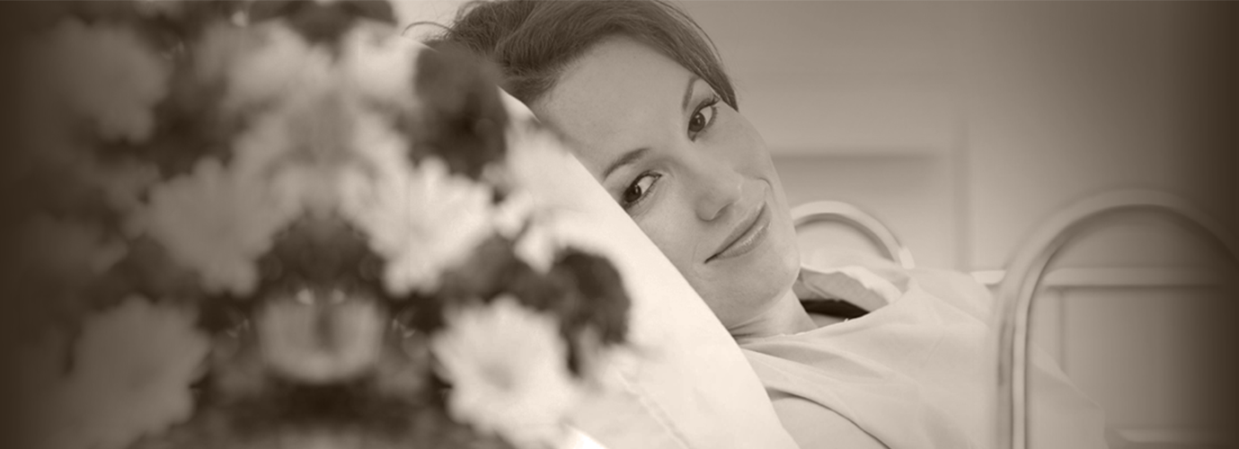 A woman lying on a stretcher looking at flowers happily in a hospital.