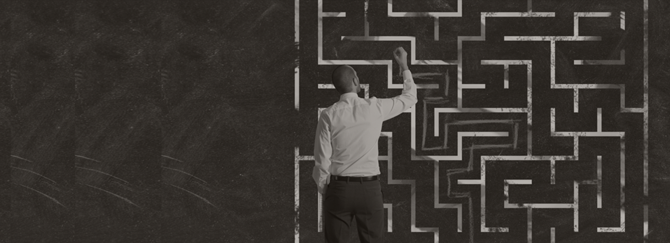A man trying to figure out solution to maze puzzle on a wall with a piece of chalk